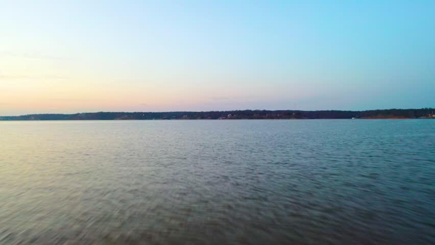 Peaceful aerial over Bull Shoals Lake, Arkansas and Missouri, showing open water, wooded Ozark hills, faint shoreline homes, and pastel dusk light over the reservoir.