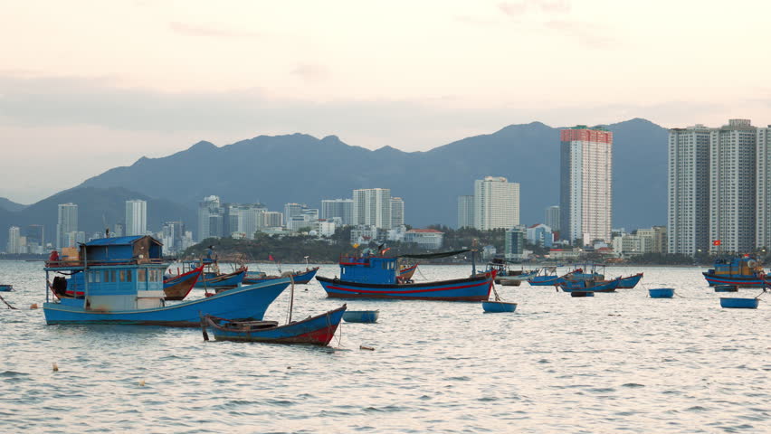Fishing boats on water with city skyline and mountains in the background during sunset in Vietnam
