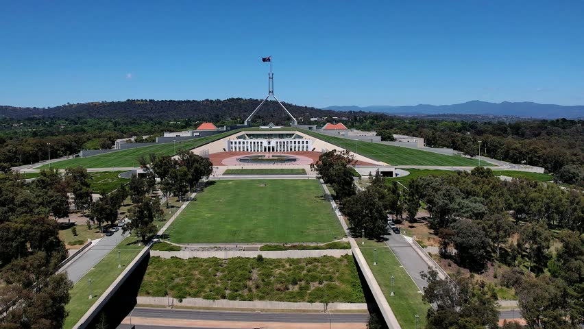 Aerial view of Parliament House with its iconic flagpole, expansive green lawns, and surrounding gardens in Canberra, Australian Capital Territory, Australia.