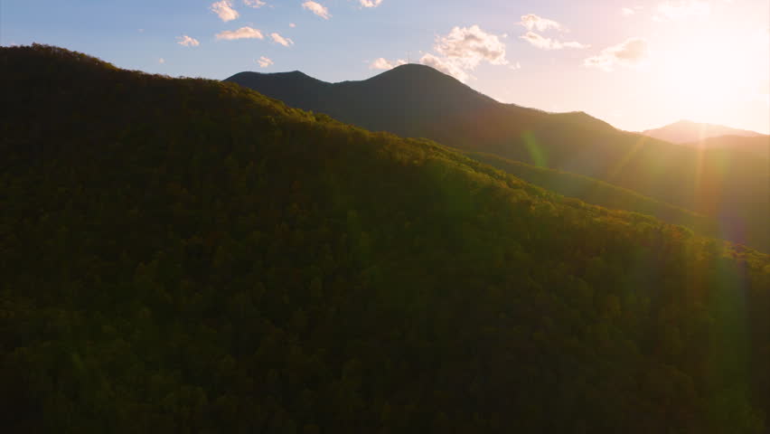 Highland woodland landscape in autumn with glowing tree canopies beneath dramatic sunset. Rich seasonal colors fill the natural mountain scenery.