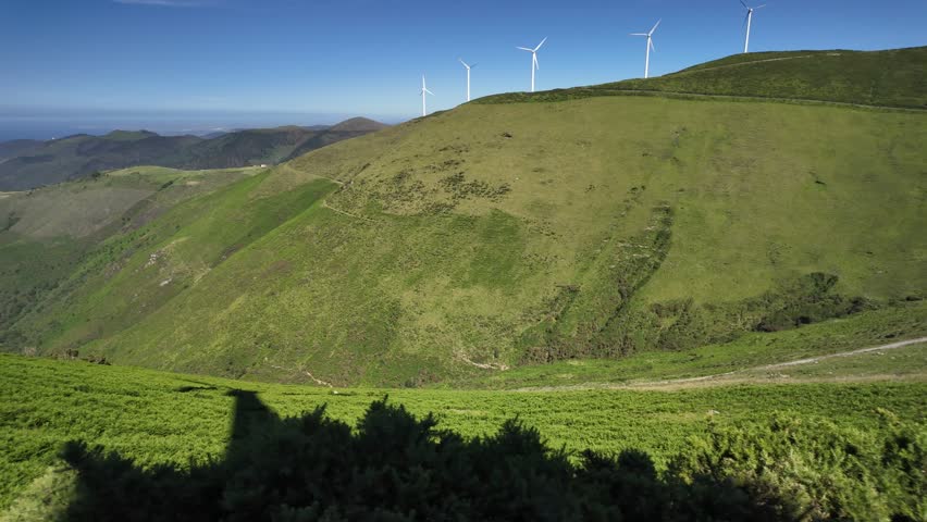 Green mountain landscape with wind turbines lined across a high ridge