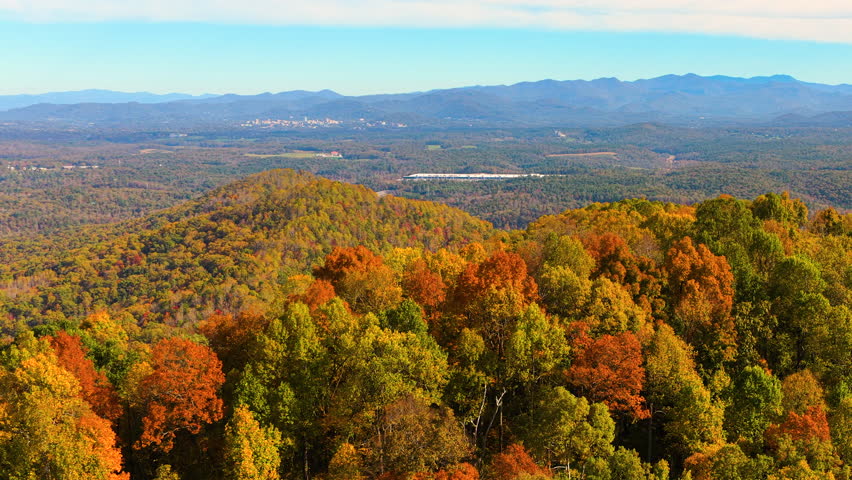 Rolling forested hills glowing with colorful autumn foliage beneath vivid sunset sky. Peaceful seasonal mountain landscape showcasing beauty of fall nature.