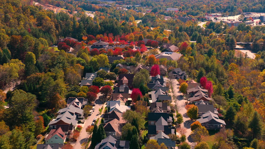 Scenic mountain community with private homes surrounded by dense woodland glowing with vibrant autumn colors. Aerial view of peaceful countryside living.