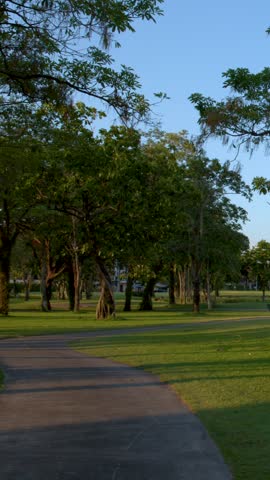 Smooth camera pan across green grass and tropical trees along a curved park walkway.