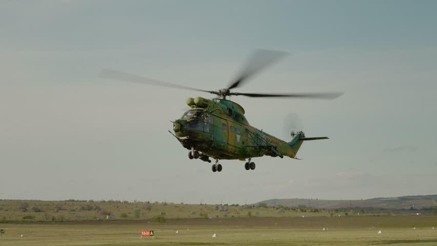 A combat helicopter lifts off the ground at an airport. The aircraft rises into the air as it prepares for flight. The environment is open with few clouds.