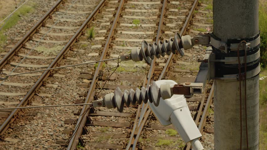 Electric wires and current dividers are shown above the railway tracks during the day. The setup highlights the infrastructure used for train operations.