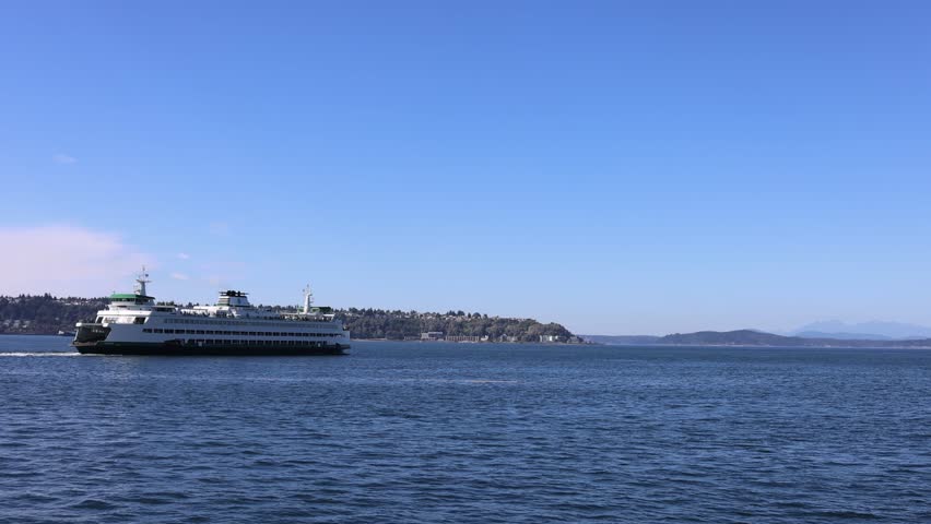 View of a ferry crossing Elliott Bay with distant hills under a clear blue sky in Seattle, Washington, United States.