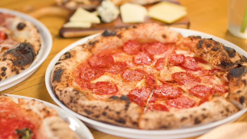People share a Neapolitan style pepperoni pizza on a wooden table in a restaurant.