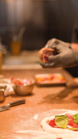 Close-up of chef in black gloves placing cured meat on pizza dough with tomato sauce.
