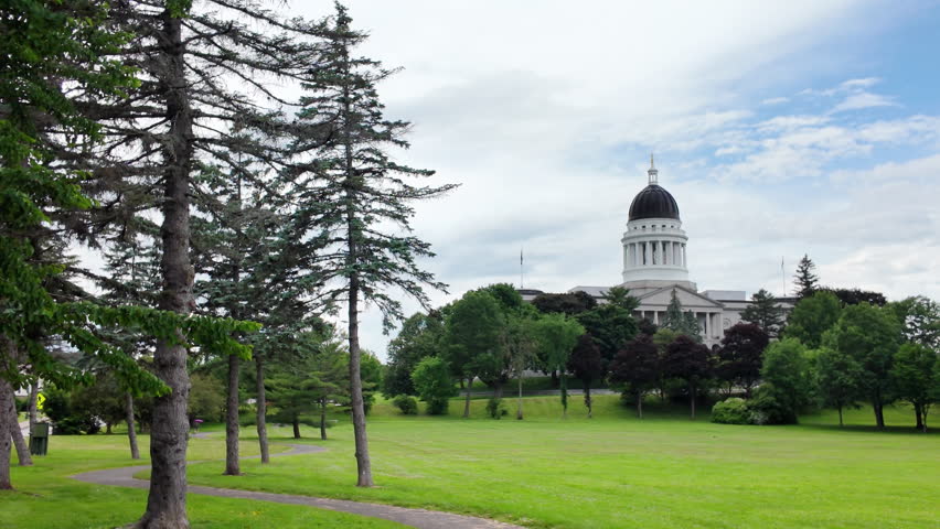 Maine State House on an overcast day with a paved footpath curving across green lawns