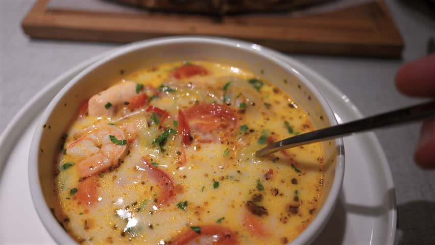 Close up of a spoon lifting shrimp from a creamy seafood soup