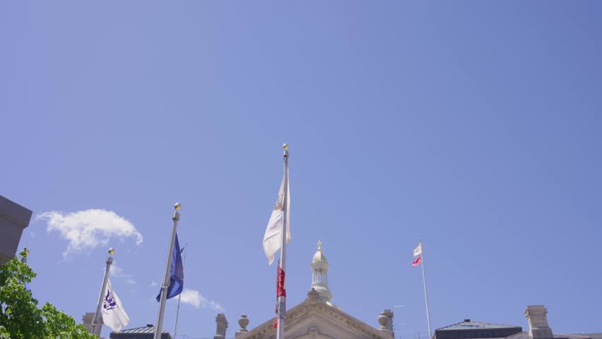 Cinematic tilt down shot from American flags revealing the New Jersey State House capitol building in downtown Trenton New Jersey on a sunny day.