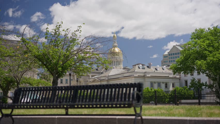 Cinematic movement shot rising up and right from a park bench to reveal the New Jersey State House capitol building in downtown Trenton New Jersey.