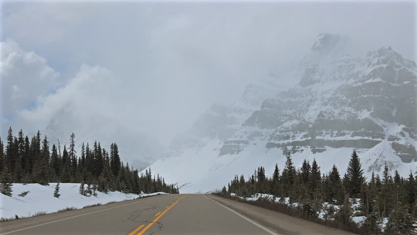 Car driver point of view video travelling along Icefields Parkway in snowy winter conditions with mountains and pine forest in Banff National Park Alberta Canada.