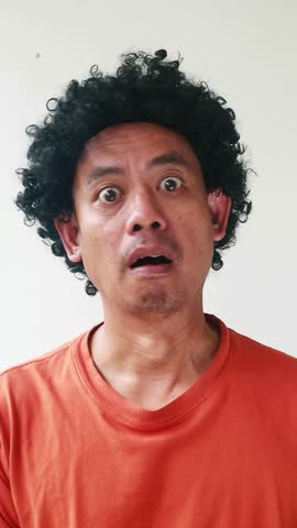 A man with a curly hair wig looking surprised and shocked at the camera.