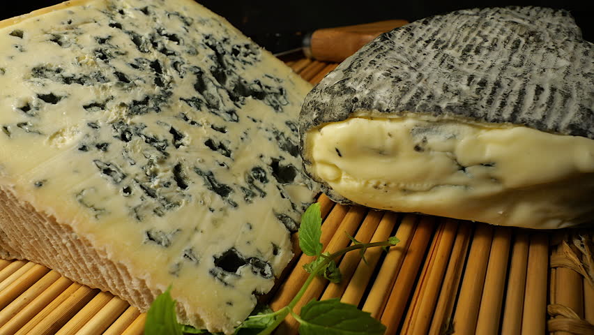 50p close up of Bleu d’Auvergne and Roche Baron cheeses displayed on a bamboo mat. Gourmet French dairy products presented in warm studio lighting
