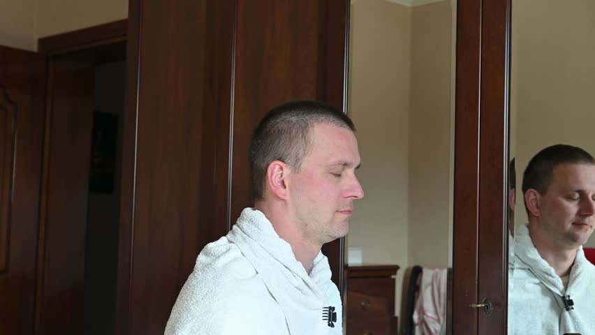 A woman gives her husband a very short buzz cut using electric hair clippers in a room at home. The video captures a casual home haircut, family life, personal grooming, and everyday domestic activities in a relaxed indoor setting.