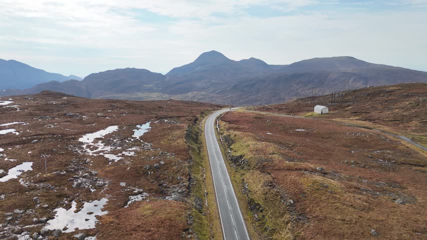 A Drone view over marsh land and road through mountains on the isle of Lewis and Harris under cloudy sky in Scotland