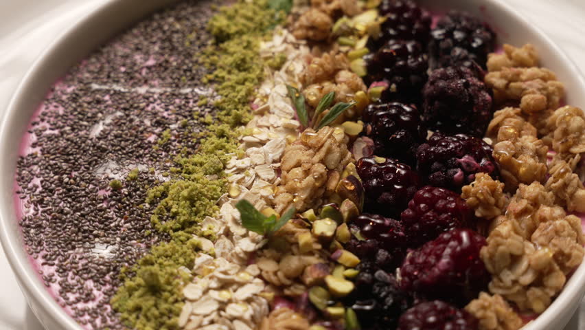 Delicious and healthy breakfast bowl rotating, with granola, berries, oats, chia seeds, and nuts, fa01