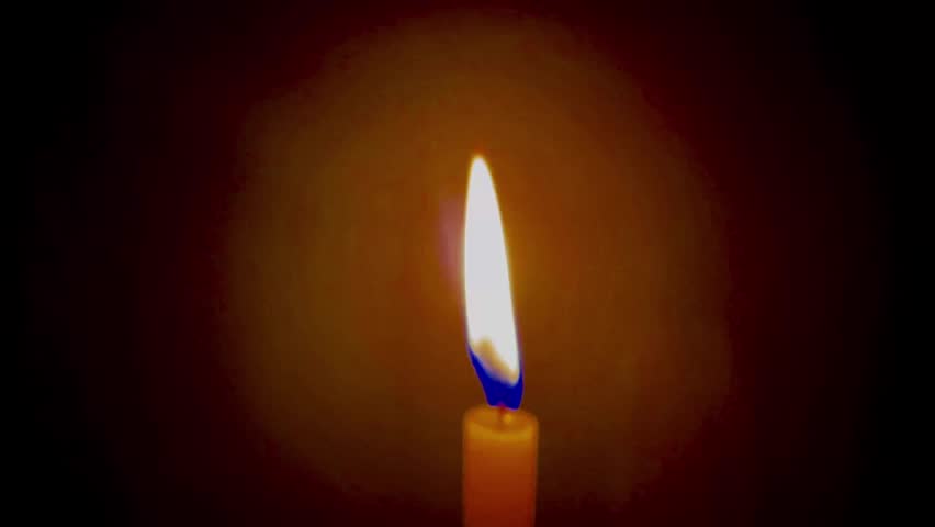 A single lit candle flickers against a dark background, its warm golden flame casting a soft glowing halo of light — video thumbnail with play button overlay.