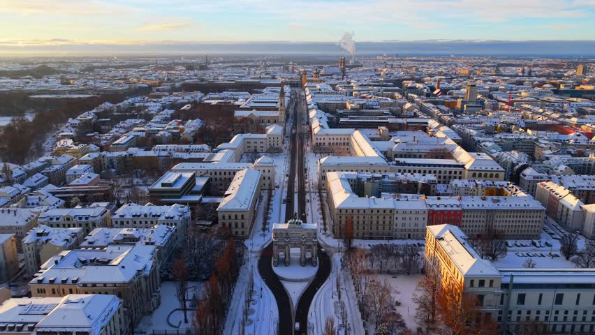 Winter drone view over Victory Gate Munich with snowy rooftops, university campus and historic boulevard. Beautiful aerial panorama of Bavaria.