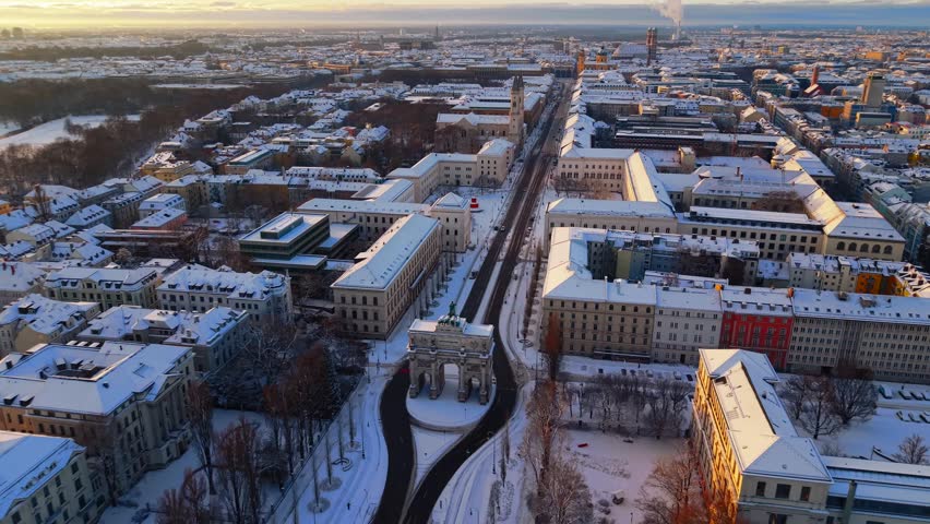 Drone footage of LMU Munich and Victory Gate in fresh snow, showing the historic boulevard, winter sunrise colors and peaceful Maxvorstadt urban panorama