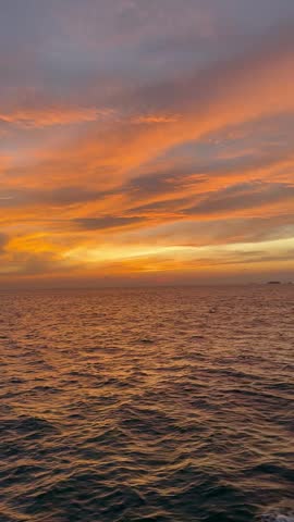 Beautiful dramatic orange sunset over the sea with golden clouds and textured water ripples.