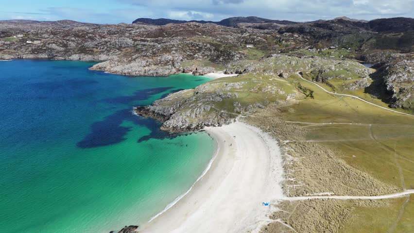 An aerial view of Achmelvich beach with rocky terrain, white sand and turquoise water on a sunny day in Scotland