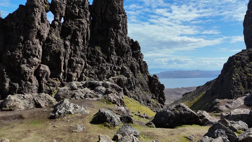 A drone rising above The Storr Hill on isle of skye surrounded by rugged landscape with blue water in the background in sunny weather in Scotland