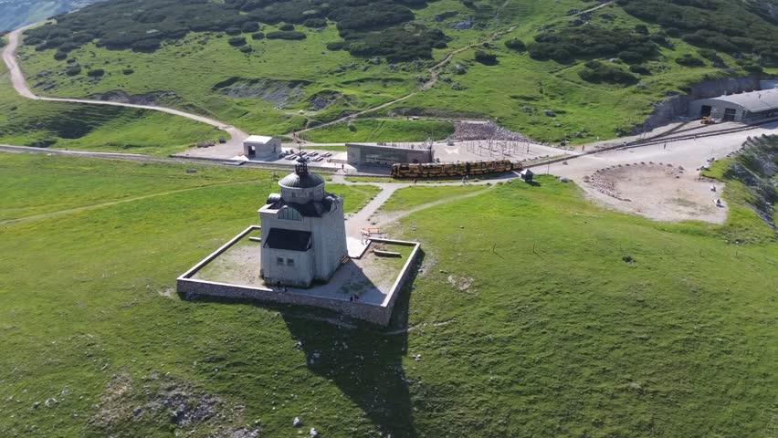 Breathtaking Aerial View of a Historic Stone Chapel on a Lush Green Mountain Peak with Winding Paths