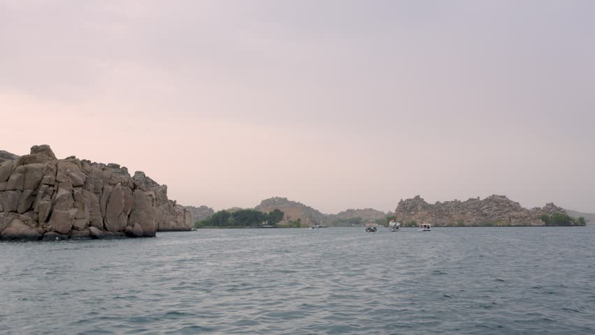 A scenic view of the ancient Philae Temple complex on Agilkia Island in Aswan, Egypt, seen from a small boat on the Nile River.