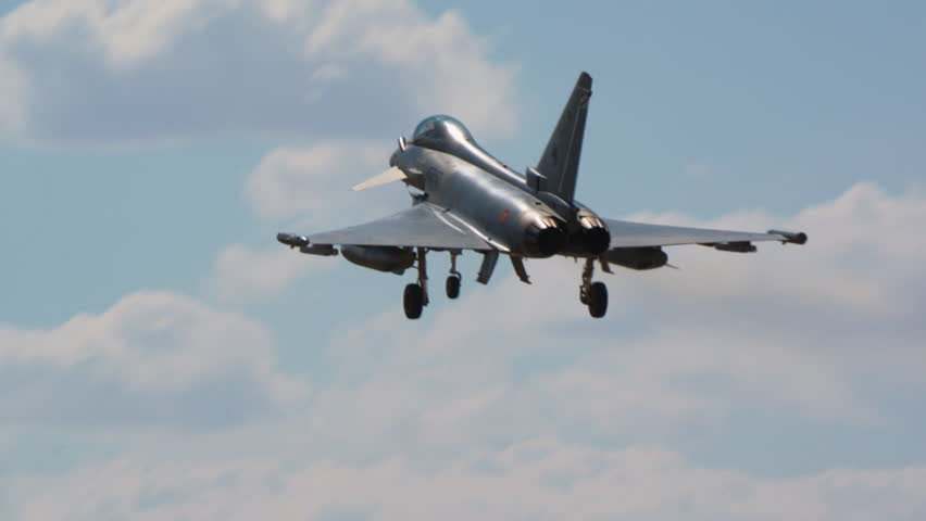 Military fighter jet climbing past a large white cloud after a go around, warplane gaining altitude against blue sky following an aborted landing, distant combat aircraft in flight