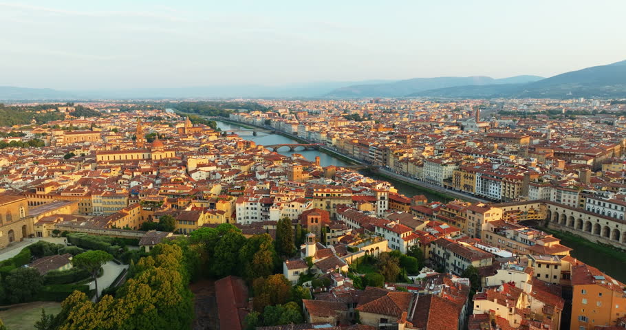Arno river winds through Florence old town golden afternoon light bridges historic buildings aerial panorama Tuscany Italy