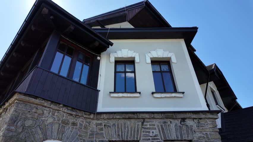 Stone foundation, white facade and brown roof of a mountain Magurka shelter captured on a sunny day with clear skies.