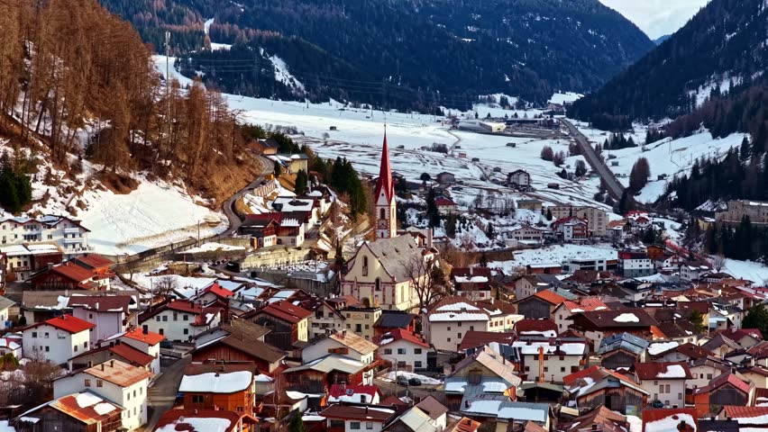 Austrian township Nauders with church tower surrounded by snow-covered mountains and houses.