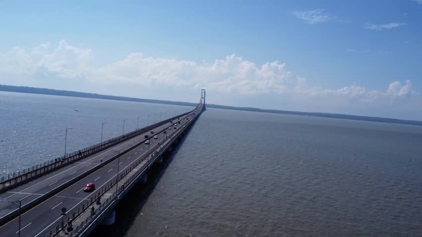 Cinematic aerial drone footage of Suramadu Bridge, the iconic bridge connecting Surabaya and Madura Island in East Java, Indonesia. Stunning panoramic view over the Madura Strait with clear blue skies, calm sea, and modern infrastructure. Perfect for travel, transportation, tourism, and urban development concepts.
