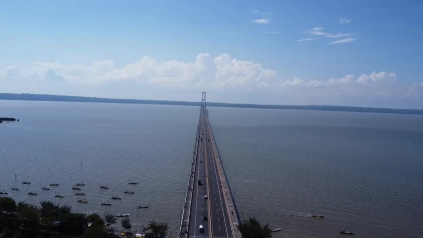 Cinematic aerial drone footage of Suramadu Bridge, the iconic bridge connecting Surabaya and Madura Island in East Java, Indonesia. Stunning panoramic view over the Madura Strait with clear blue skies, calm sea, and modern infrastructure. Perfect for travel, transportation, tourism, and urban development concepts.
