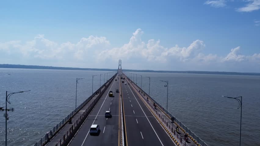 Cinematic aerial drone footage of Suramadu Bridge, the iconic bridge connecting Surabaya and Madura Island in East Java, Indonesia. Stunning panoramic view over the Madura Strait with clear blue skies, calm sea, and modern infrastructure. Perfect for travel, transportation, tourism, and urban development concepts.