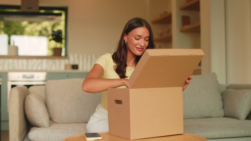 Smiling young woman unpacking cleaning products from cardboard parcel at home, 4K