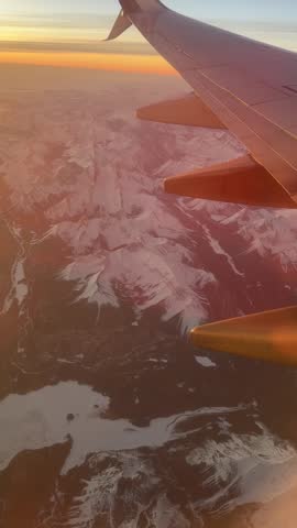 Airplane wing over glacier valley in Canadian Rockies near Banff, golden light aerial view