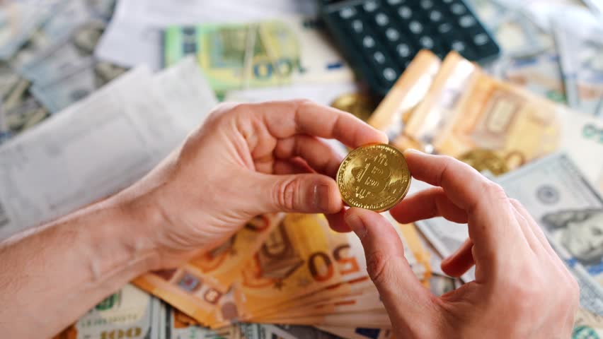 Hands shows silver and golden BTC bitcoin against the dollars and euros