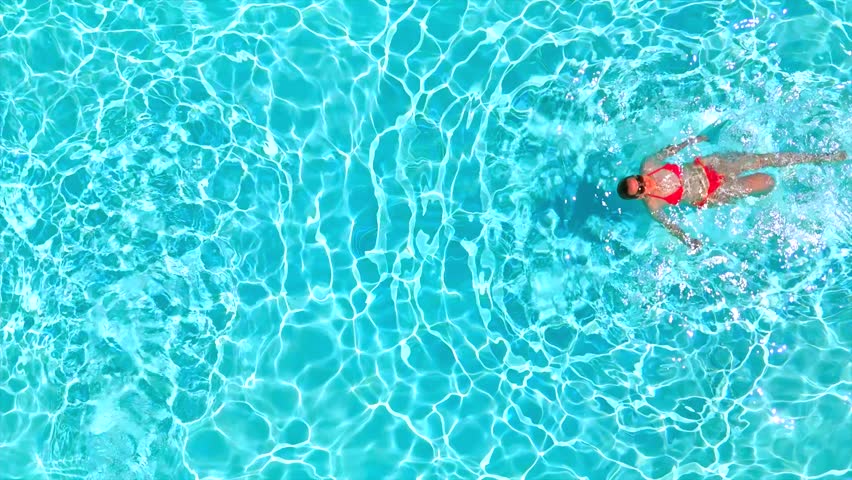 Top down view of a woman in pink swimsuit swimming on her back in the pool.