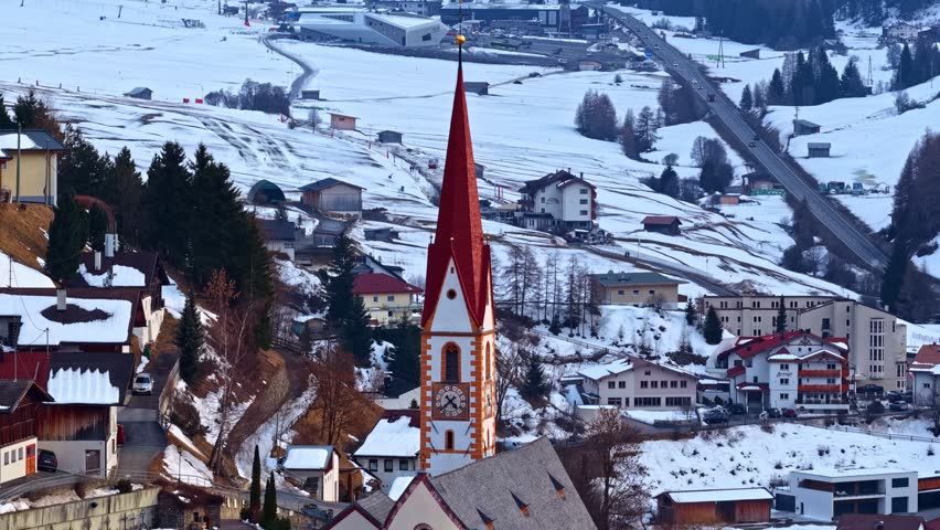 Church tower in Nauders, Austria with snow covered village and winter landscape.