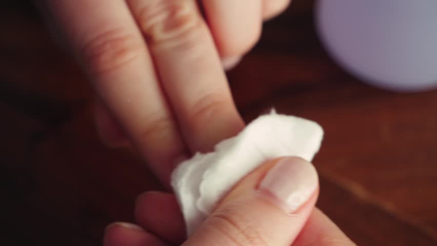 Close-up of hands removing nail polish with a cotton pad and nail polish remover. Beauty routine, manicure care, personal grooming, and self-care concept at home. High quality 4k footage