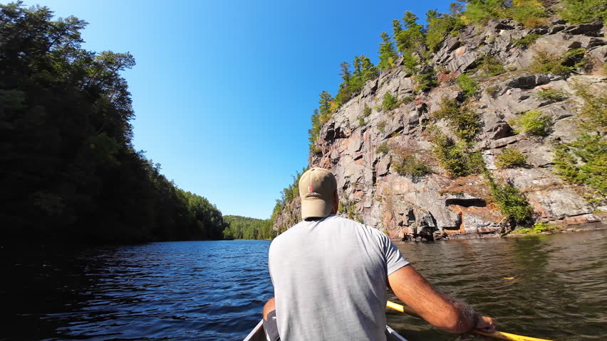 Man paddling a canoe along the river below the dramatic cliffs of Barron Canyon in Algonquin Provincial Park, Ontario, Canada.