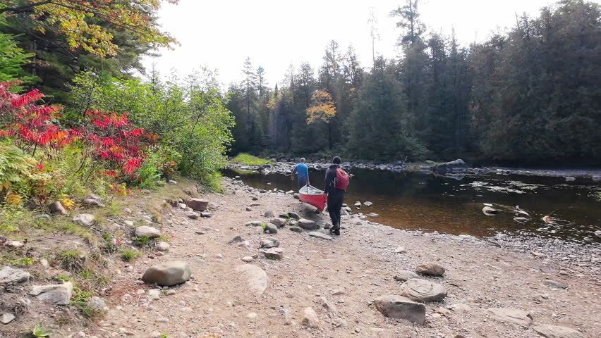 Two men complete a canoe portage and set the canoe down near the shoreline before launching on a river in the Algonquin Park region of Ontario, Canada.