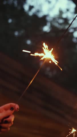 Vertical video. Hand holding burning sparkler during outdoor wedding celebration at night.