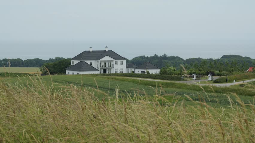 Scenic view of a large white house in a rural landscape with tall grass swaying in the wind