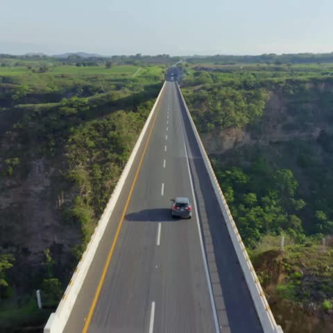 A drone shot of a highway bridge with cars passing by, centered in a stunning landscape of green hills. Perfect for nature, travel, or scenic content.