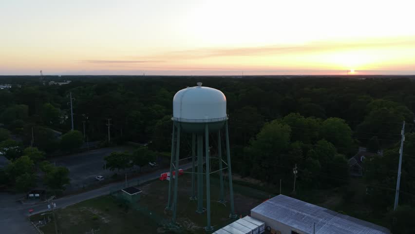 Water tower stands tall against a sunset backdrop, surrounded by trees and a quiet neighborhood in Myrtle Beach, South Carolina